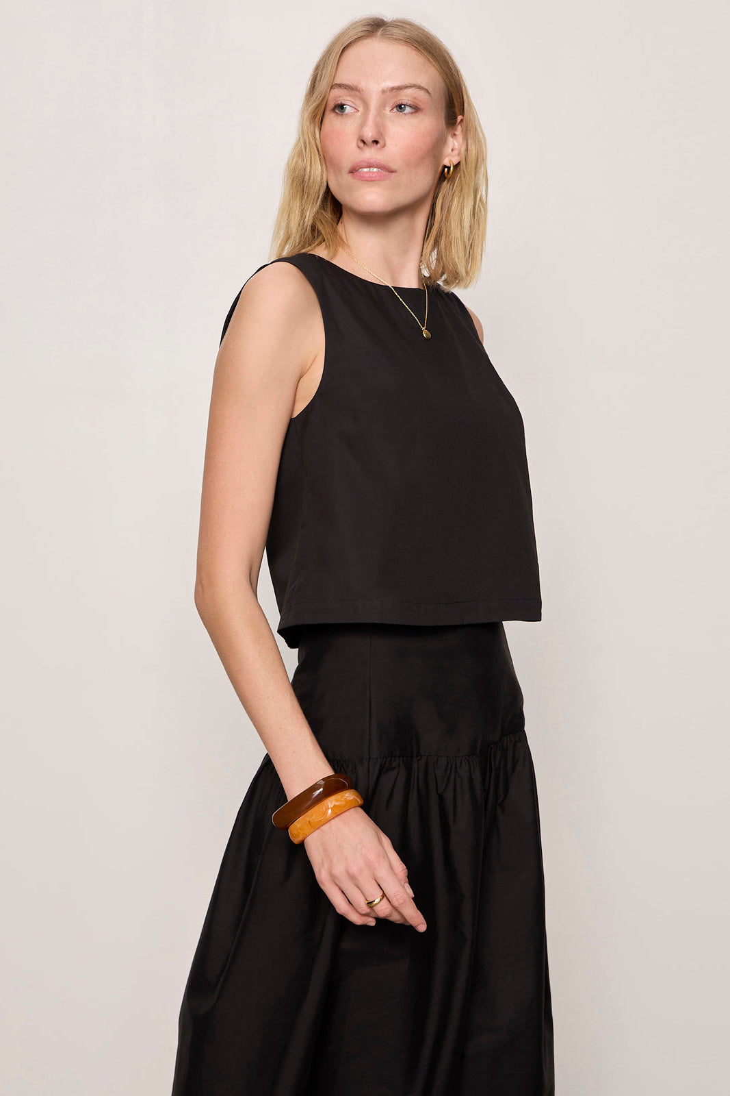 Woman wearing a black sleeveless top and black skirt against a plain background