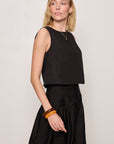 Woman wearing a black sleeveless top and black skirt against a plain background