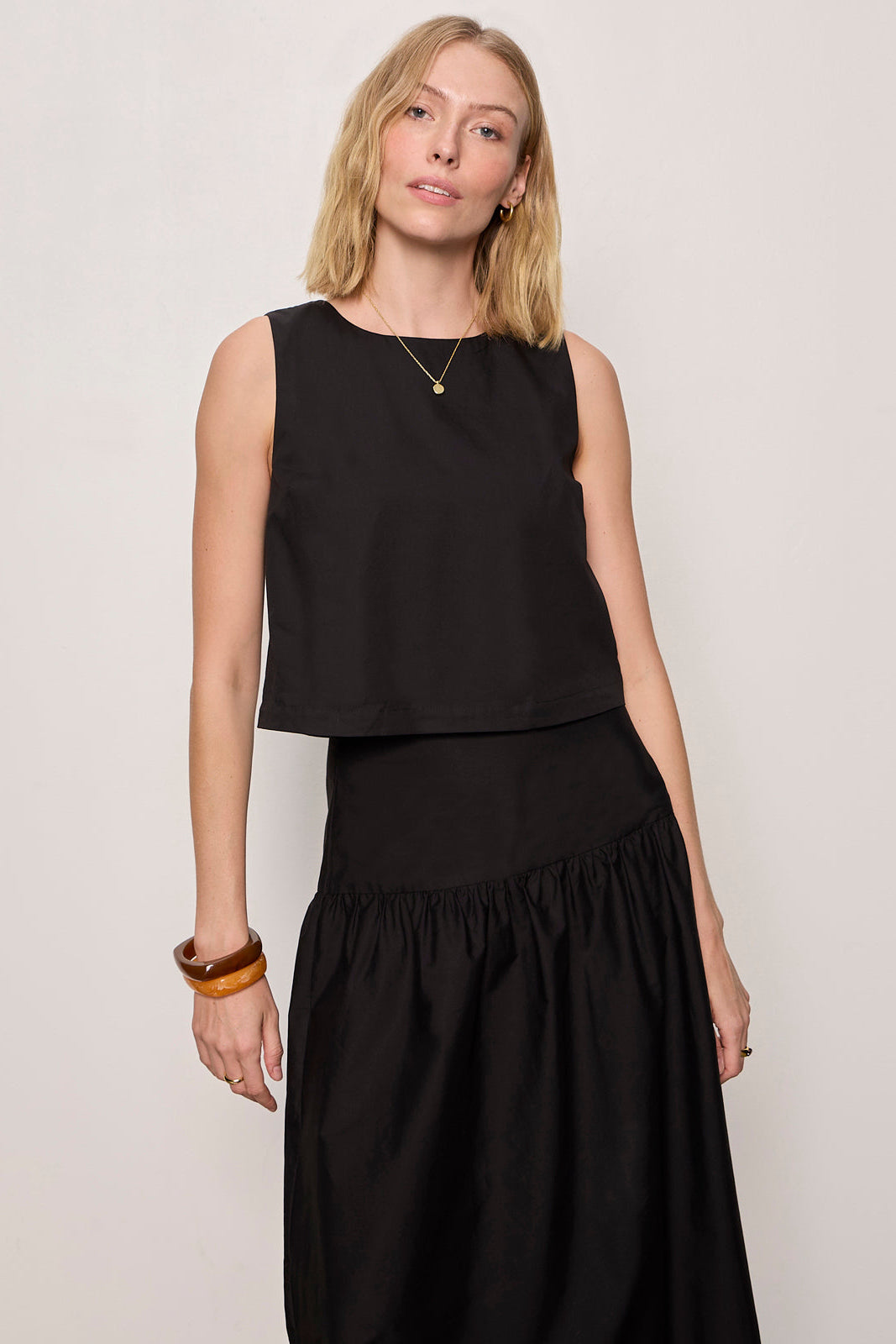 Woman wearing a black sleeveless top and skirt against a plain background
