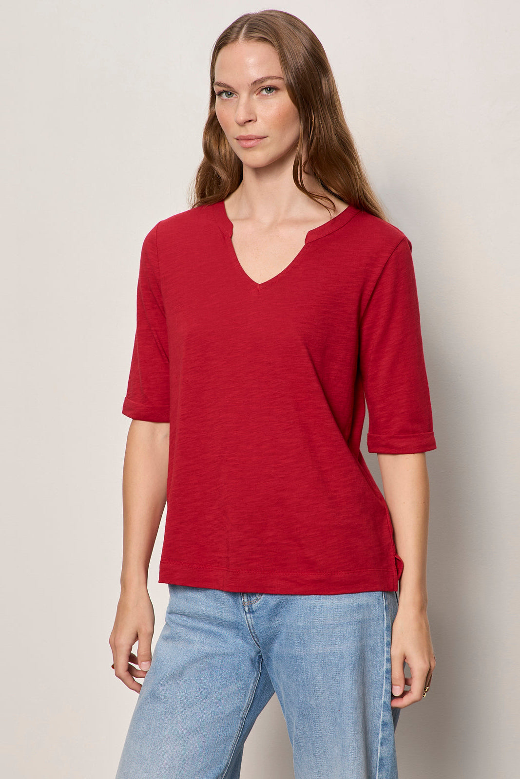 Woman wearing a red shirt and blue jeans against a plain background