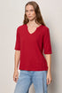Woman wearing a red shirt and blue jeans against a plain background