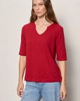 Woman wearing a red shirt and blue jeans against a plain background