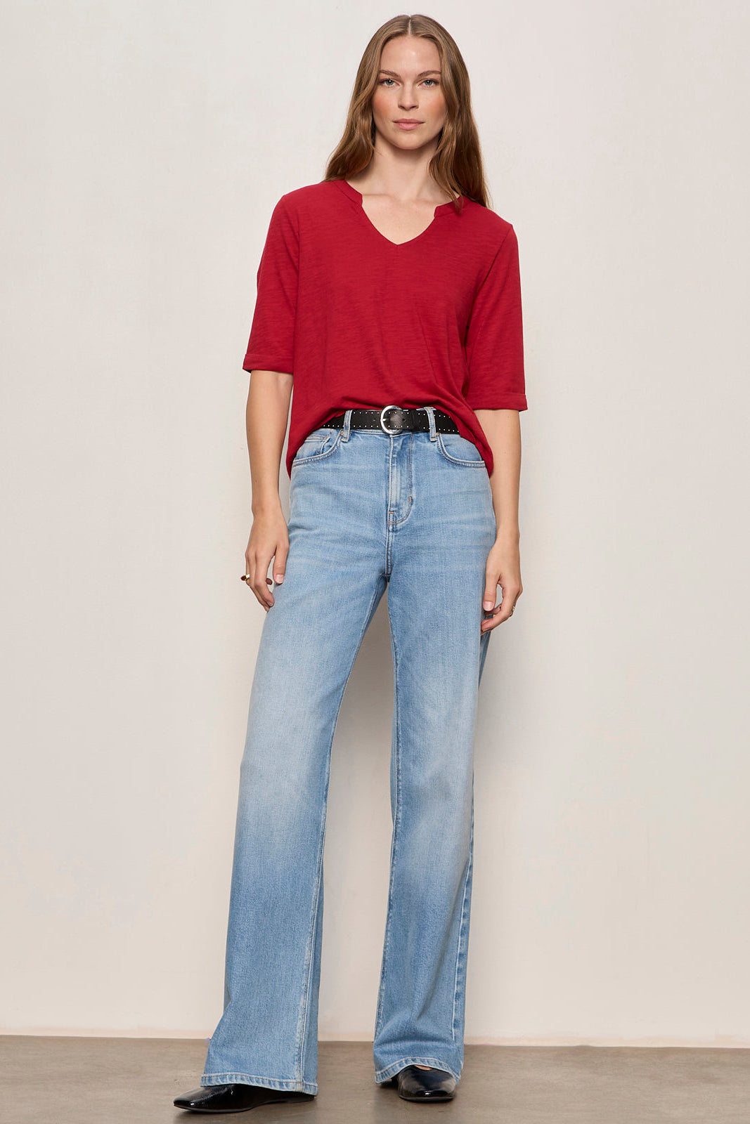 Woman wearing a red shirt and blue jeans against a plain background