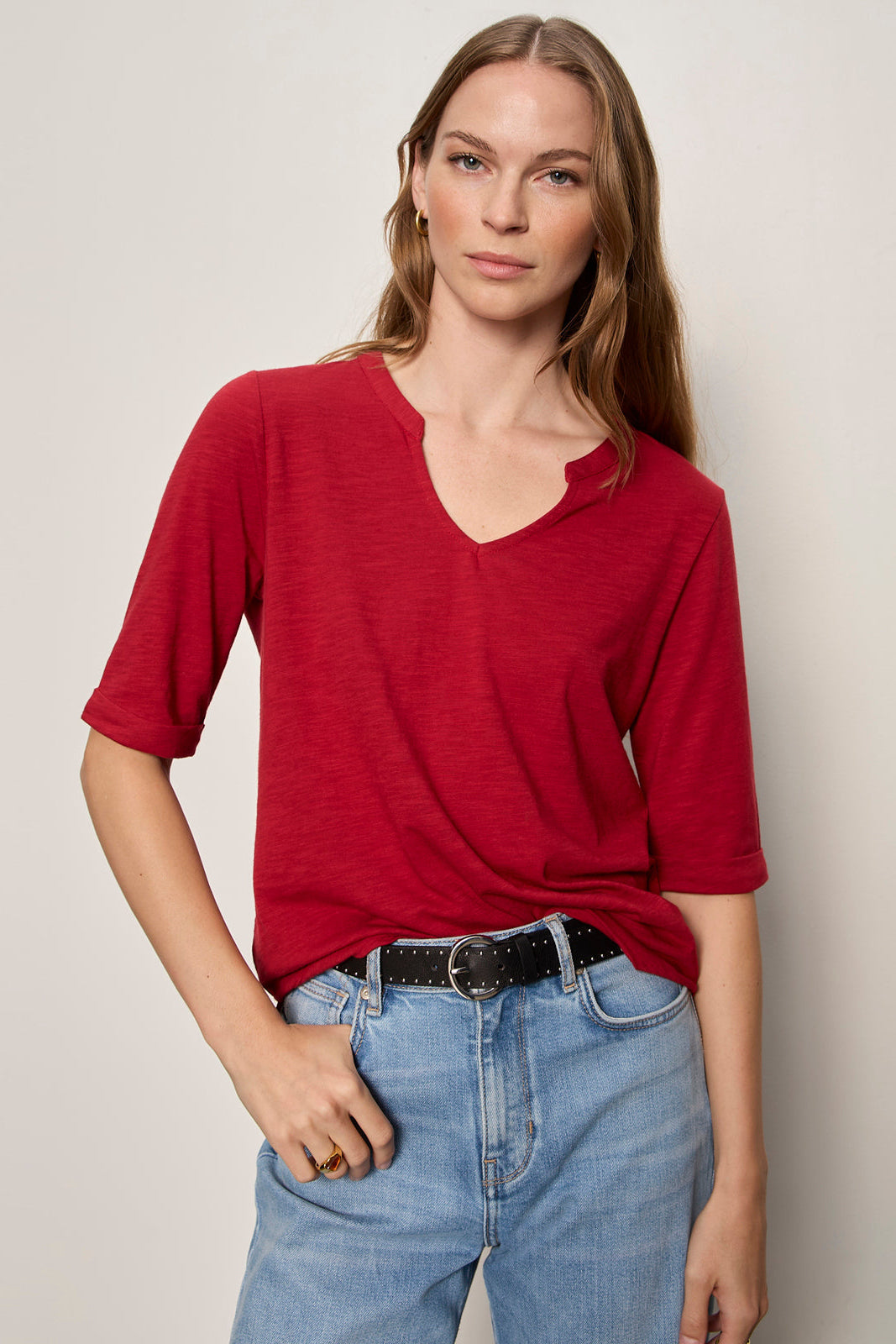 Woman wearing a red shirt and blue jeans against a plain background