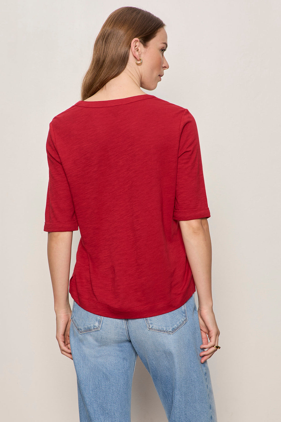 Woman wearing a red shirt and blue jeans on a plain background