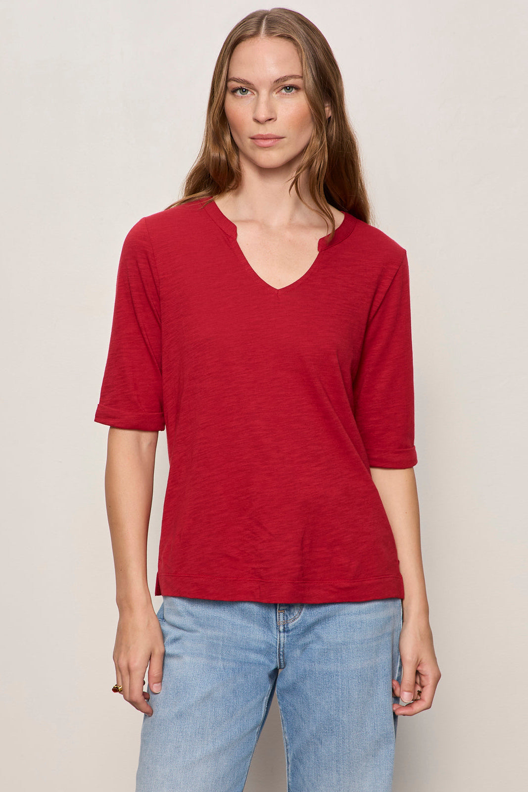 Woman wearing a red shirt and blue jeans against a plain background