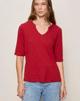 Woman wearing a red shirt and blue jeans against a plain background