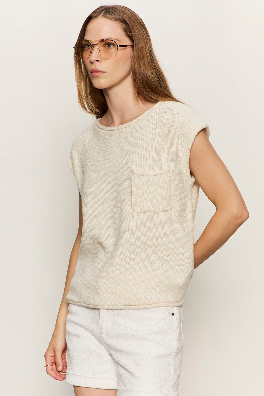 Woman wearing a beige sleeveless top with a pocket on a plain background