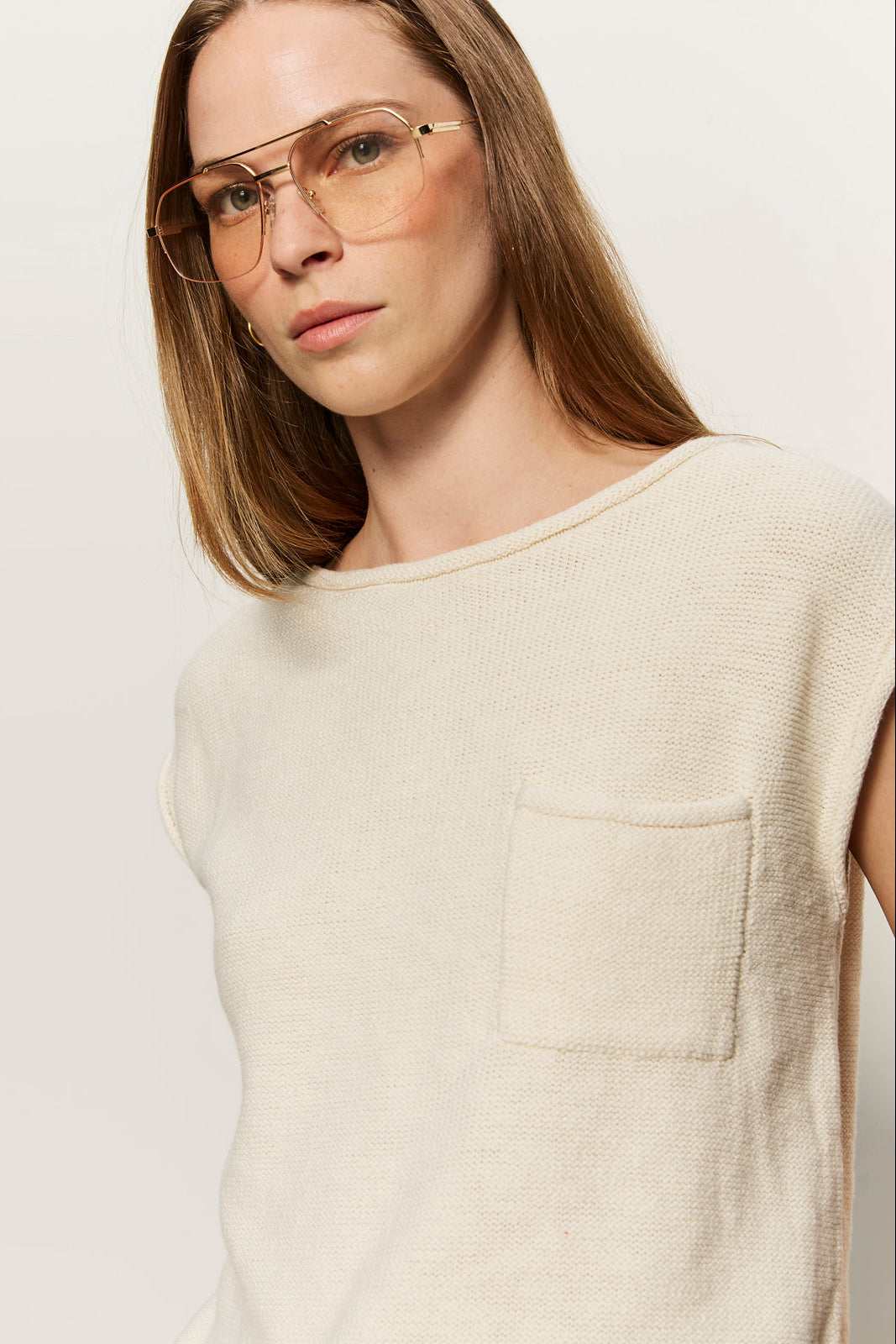 Woman wearing a beige sleeveless sweater against a plain background