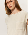 Woman wearing a beige sleeveless sweater against a plain background