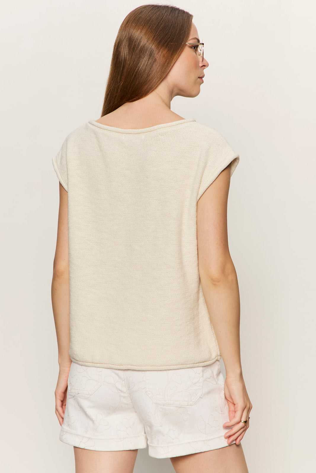 Woman wearing a beige top and white shorts on a plain background