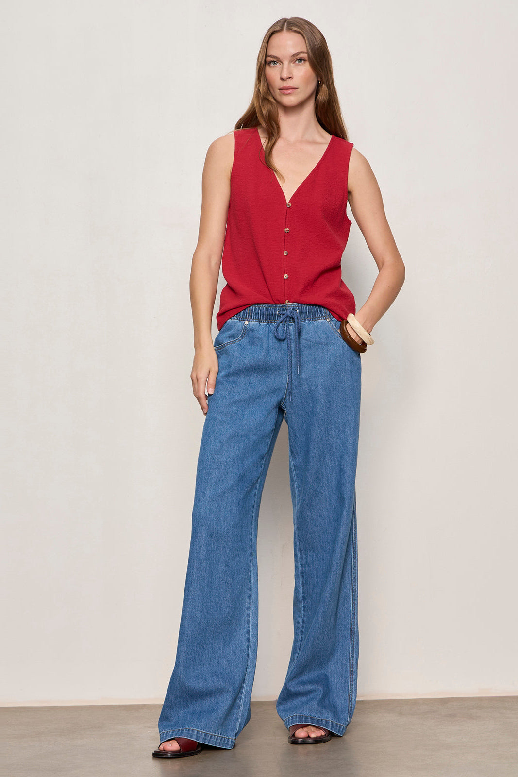 Woman wearing a red sleeveless top and blue jeans against a plain background