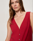 Woman wearing a red sleeveless top with buttons on a plain background