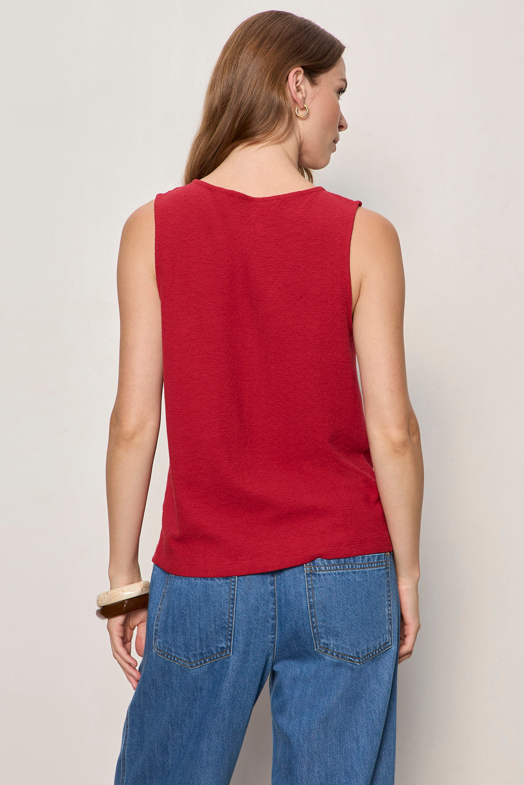 Person wearing a red sleeveless top and blue jeans on a plain background