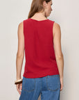 Person wearing a red sleeveless top and blue jeans on a plain background
