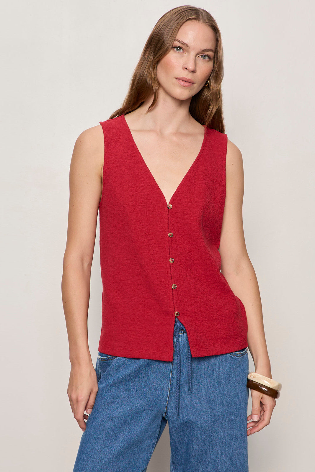 Woman wearing a red sleeveless top and blue pants on a plain background