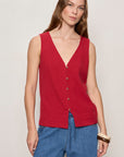 Woman wearing a red sleeveless top and blue pants on a plain background