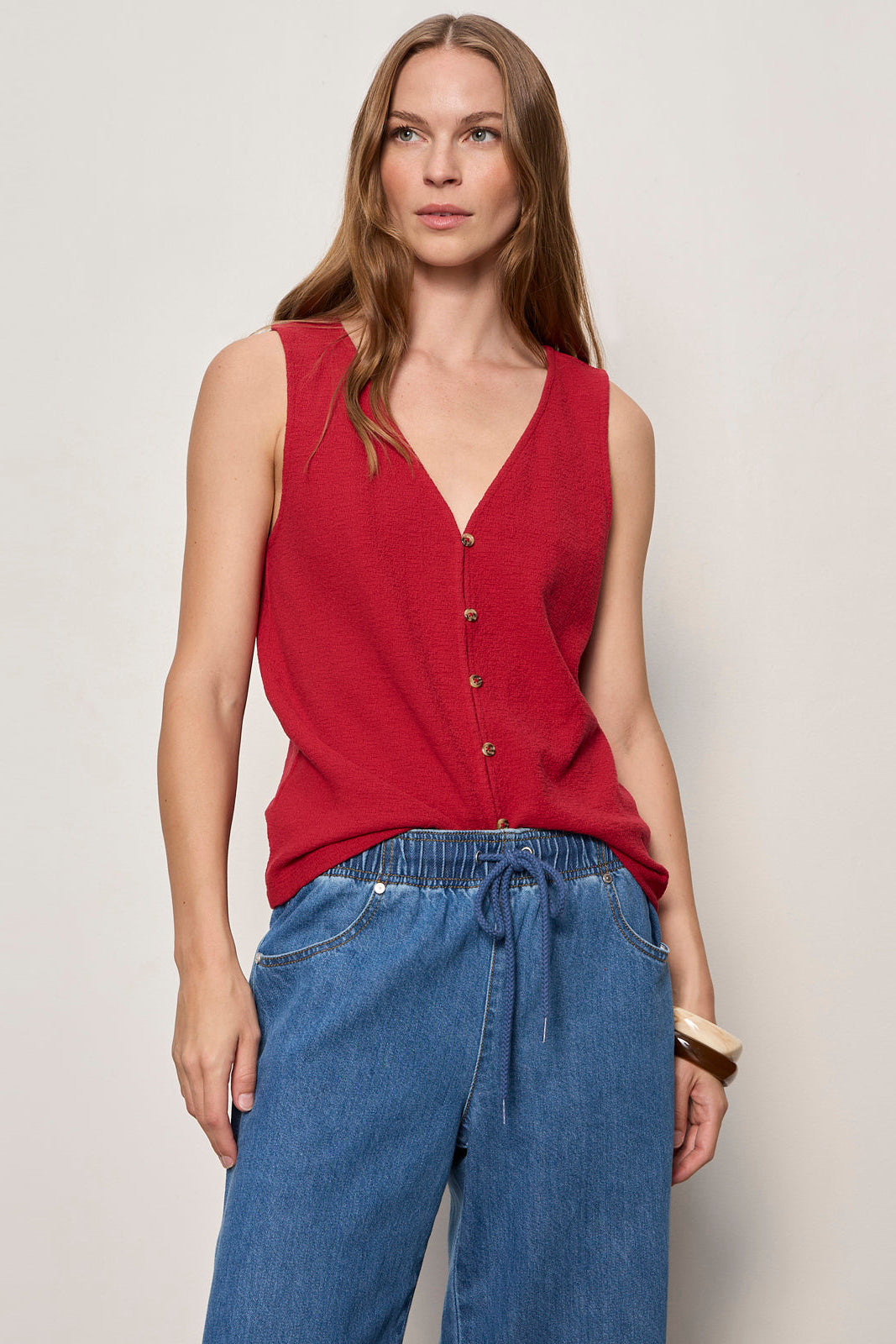 Woman wearing a red sleeveless top and blue jeans against a plain background