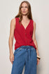 Woman wearing a red sleeveless top and blue jeans against a plain background
