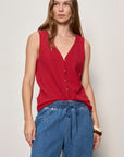 Woman wearing a red sleeveless top and blue jeans against a plain background