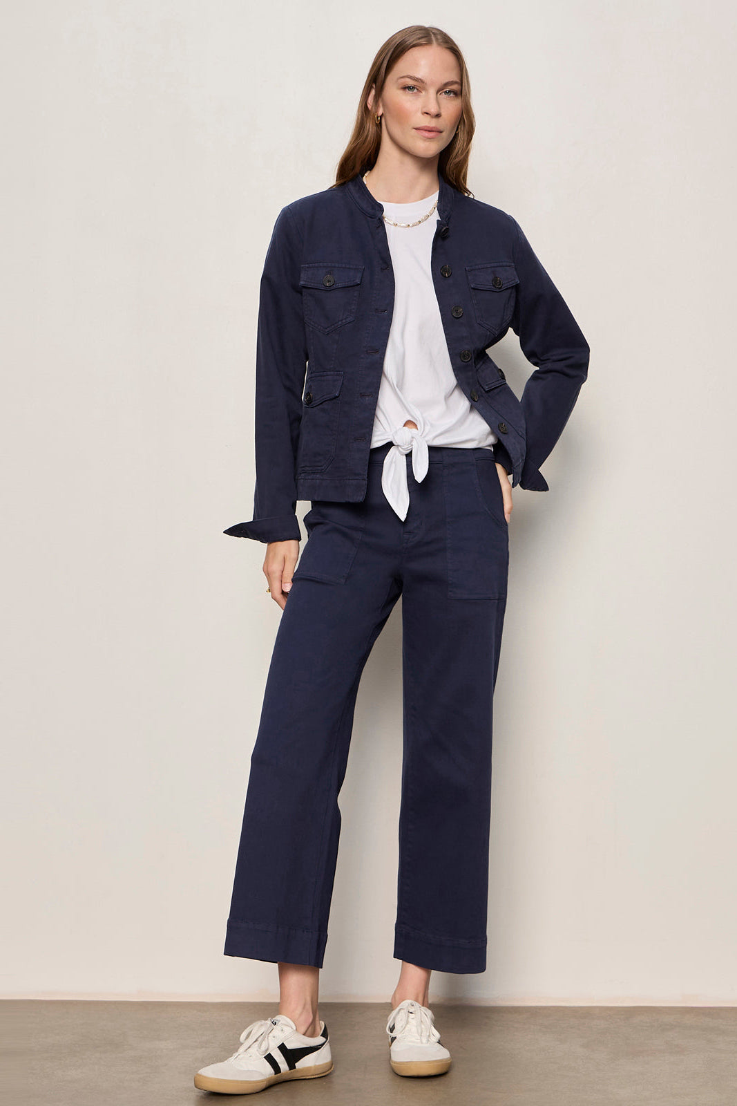 Woman wearing a navy jacket and pants with a white shirt, standing against a plain background.