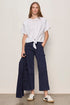 Woman wearing a white top and navy pants against a plain background