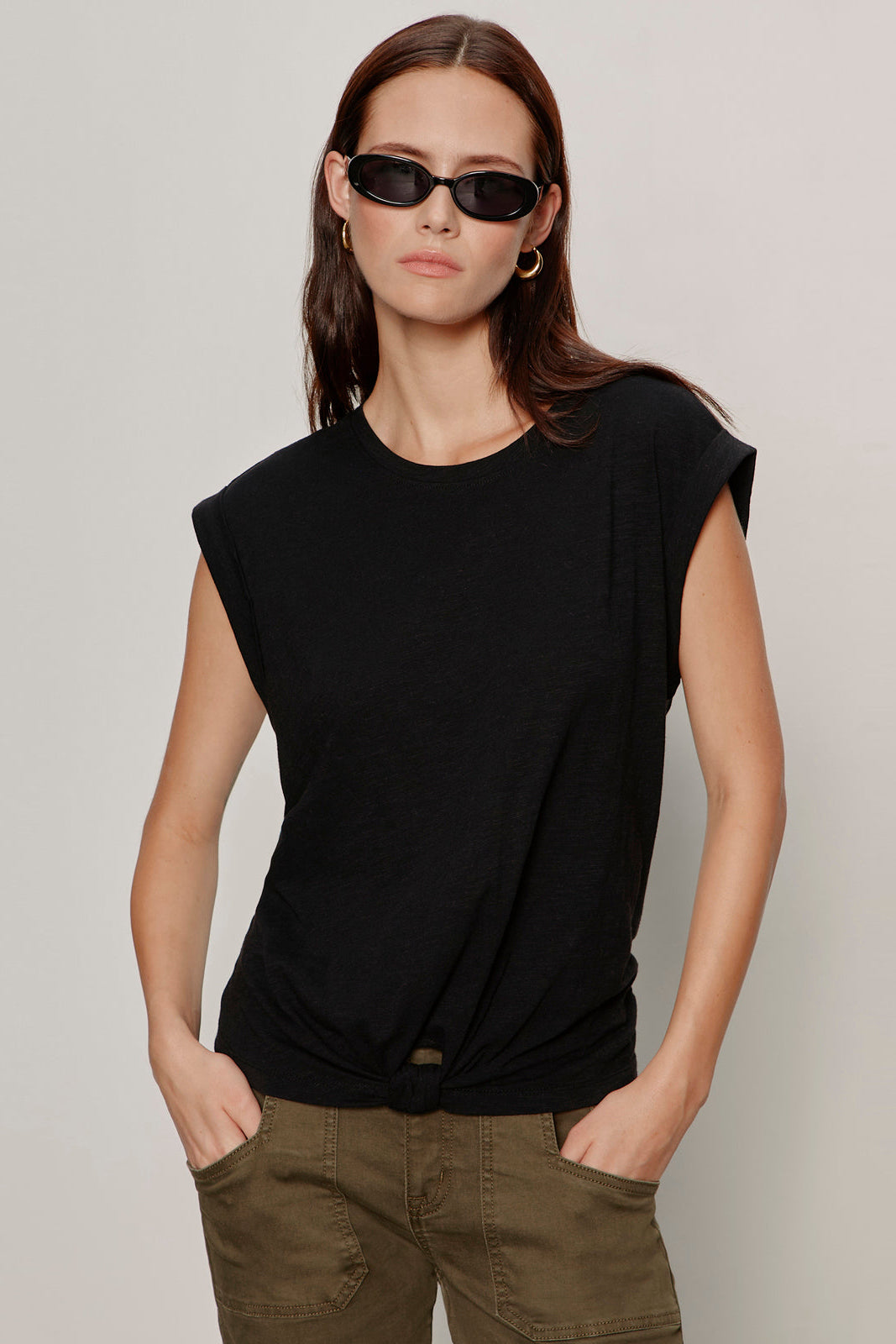 Woman wearing a black sleeveless top and green pants against a plain background
