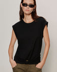 Woman wearing a black sleeveless top and green pants against a plain background