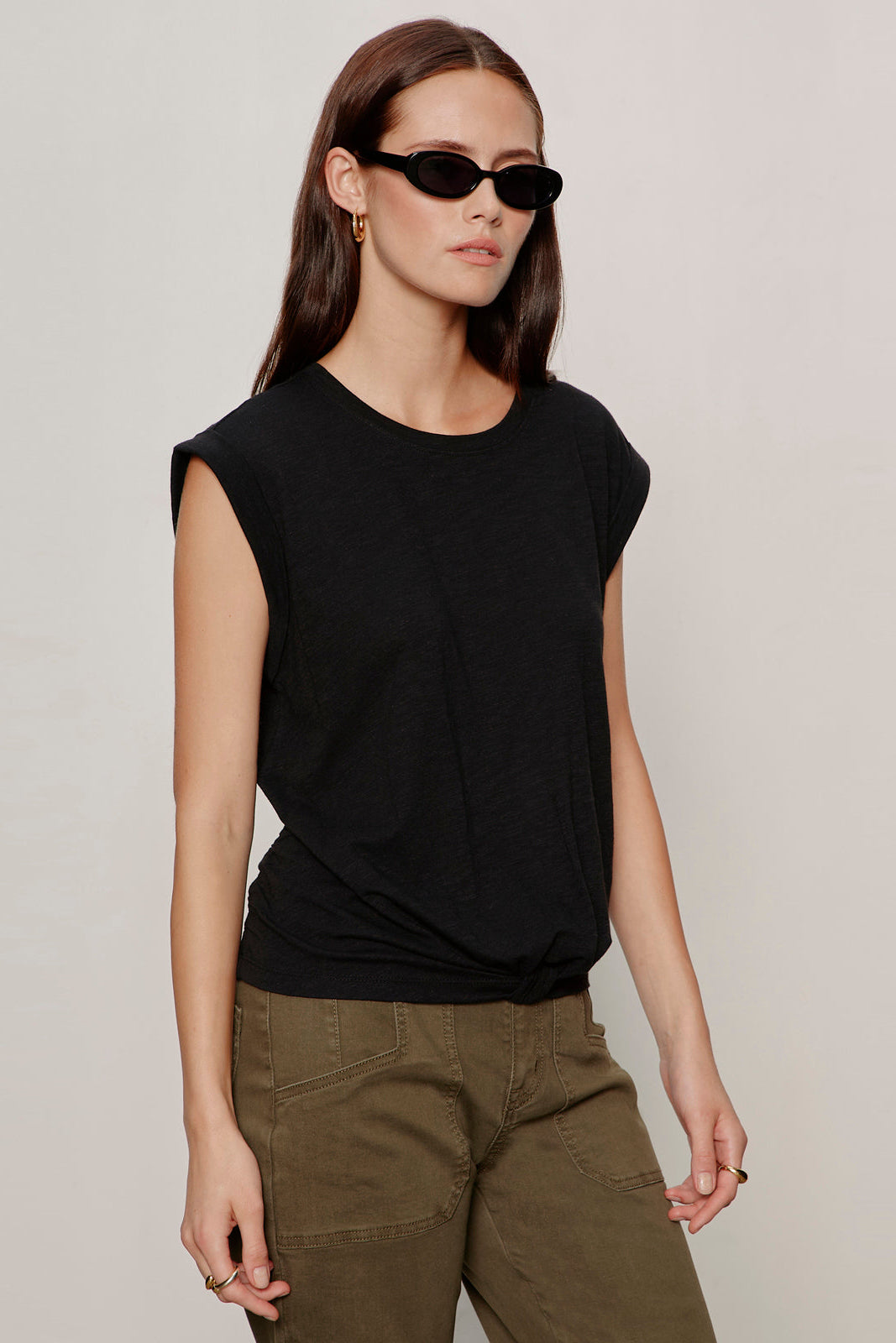 Woman wearing a black sleeveless top and green pants against a plain background