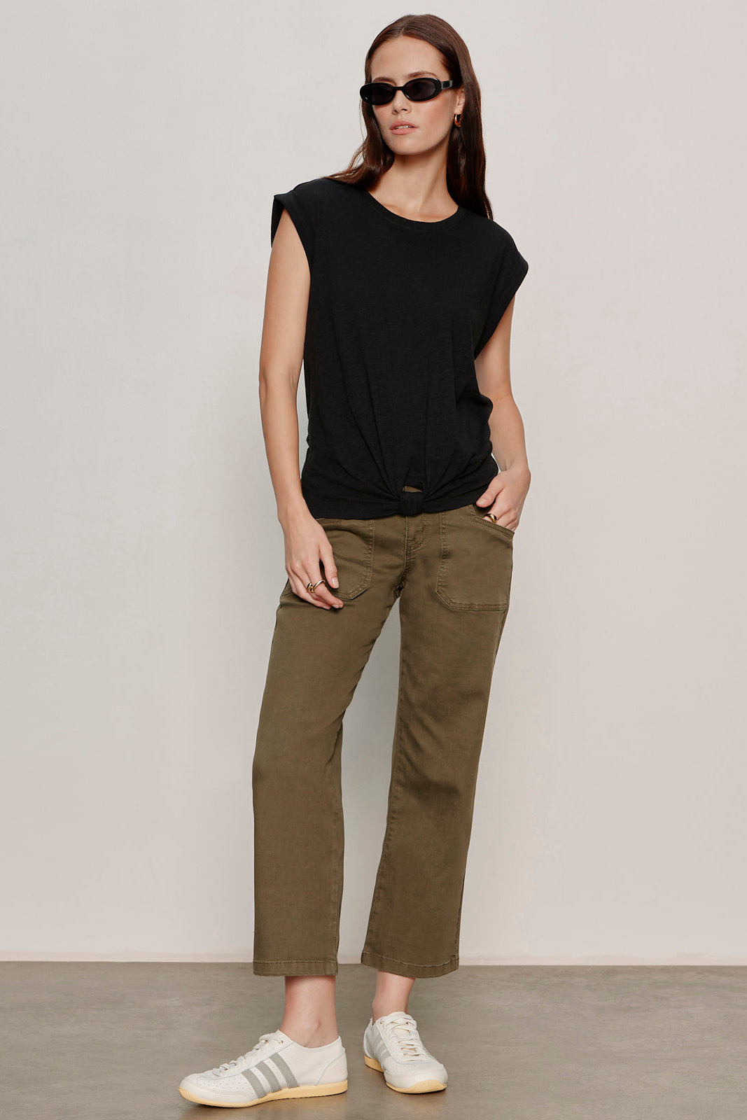 Woman wearing a black sleeveless top and olive green pants against a plain background