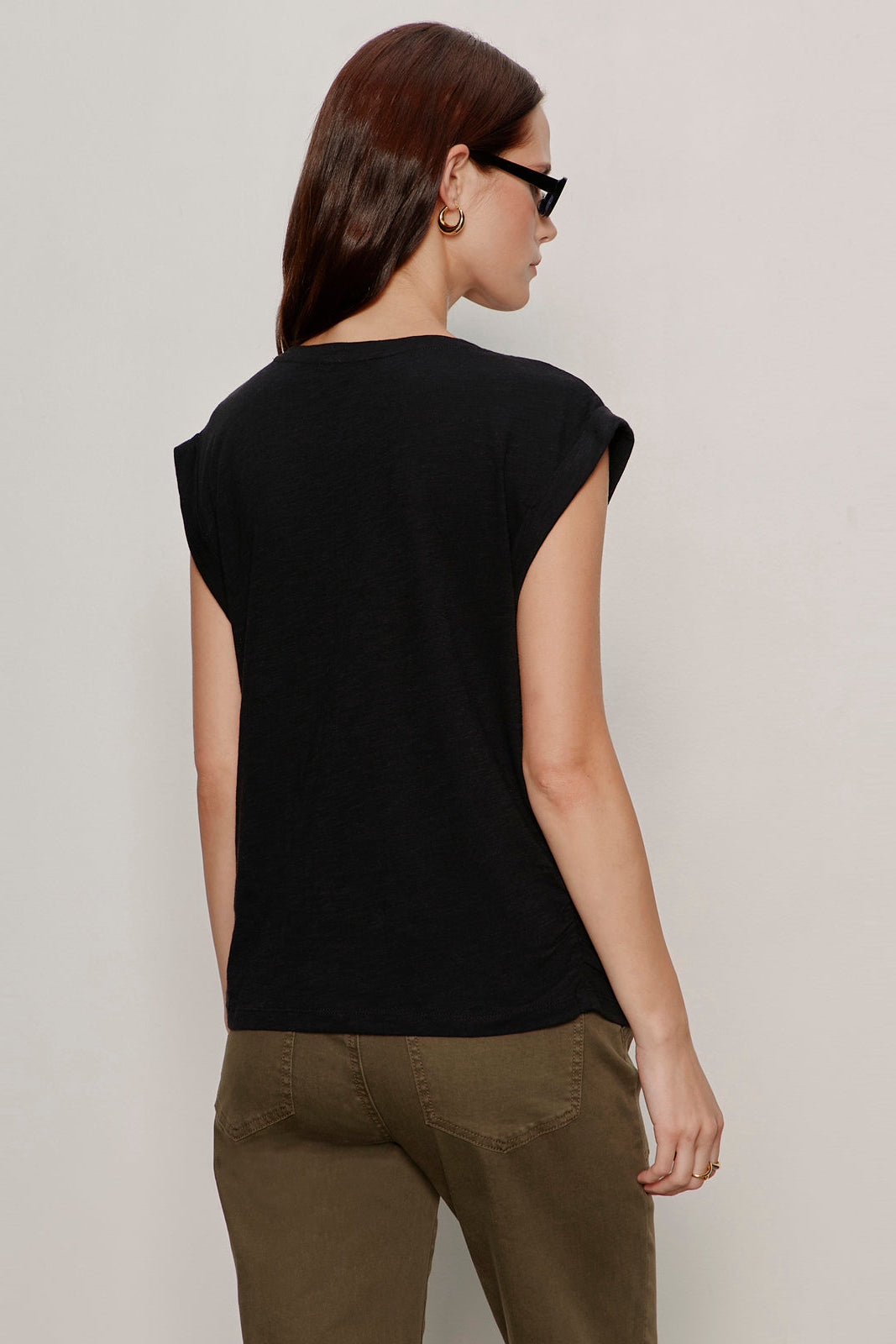 Woman wearing a black sleeveless top and brown pants against a plain background