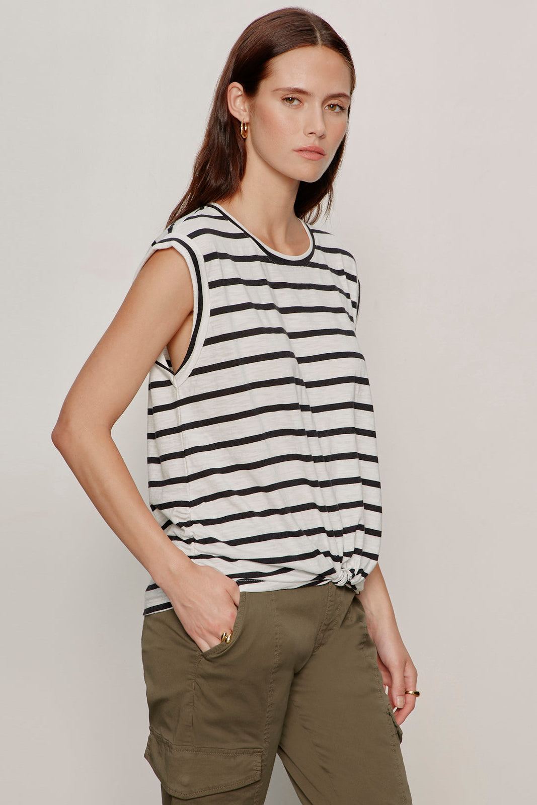 Woman wearing a black and white striped sleeveless top and green cargo pants on a plain background