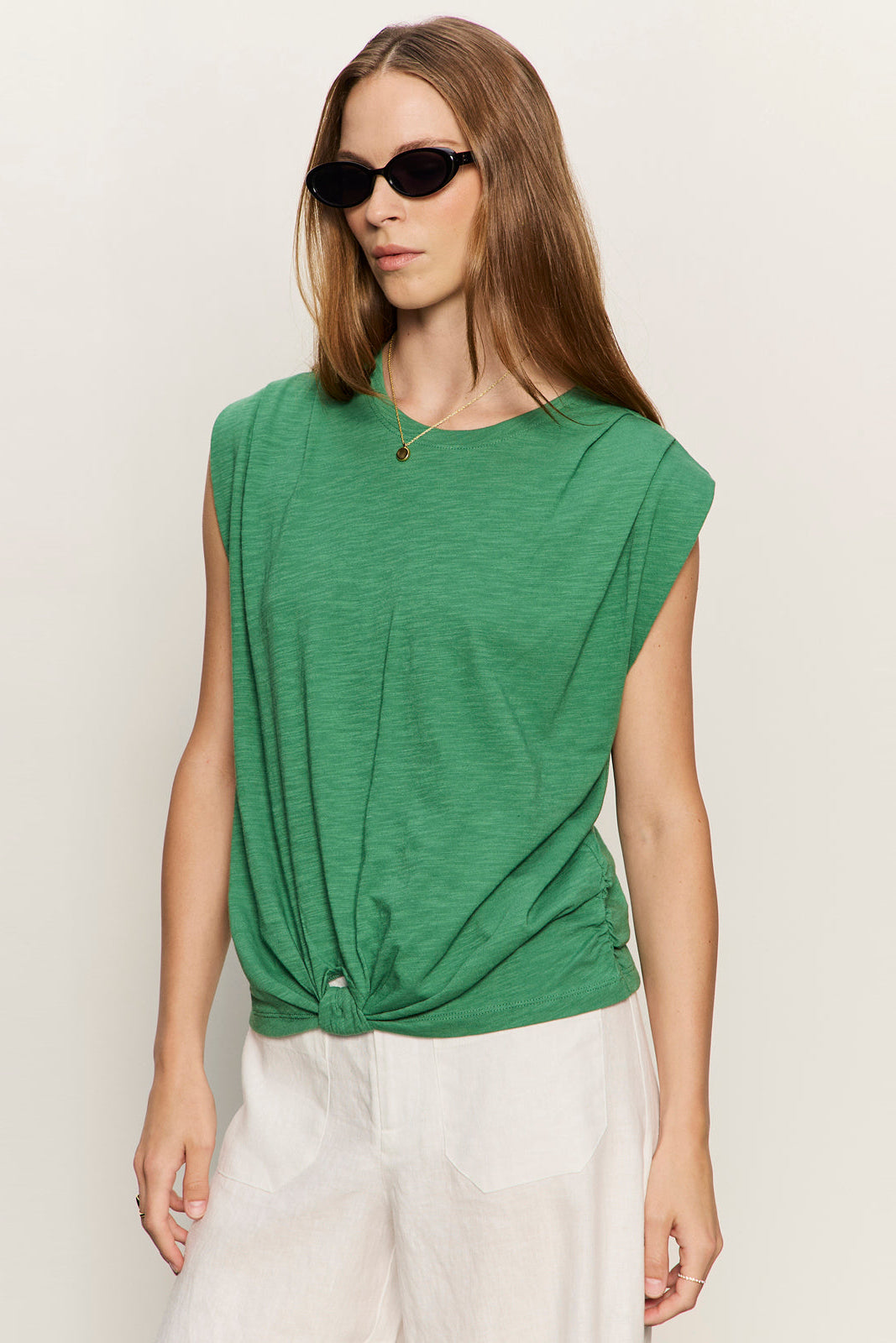Woman wearing a green top and white pants against a plain background