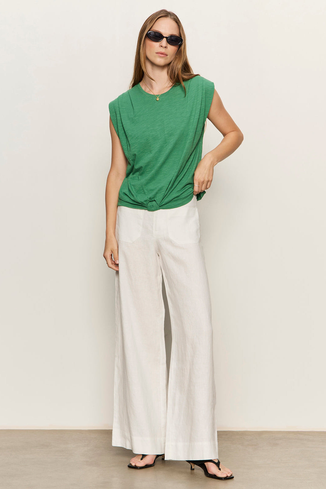 Woman wearing a green top and white pants against a plain background