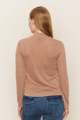 Woman wearing a brown long-sleeve top and blue jeans on a beige background