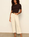 Woman wearing a black top and white pants against a plain background
