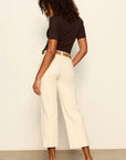 Woman wearing a black top and beige pants against a plain background