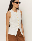Woman wearing a white sleeveless button-up top and brown shorts against a plain background