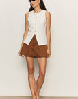 Woman wearing a white sleeveless top and brown shorts against a plain background