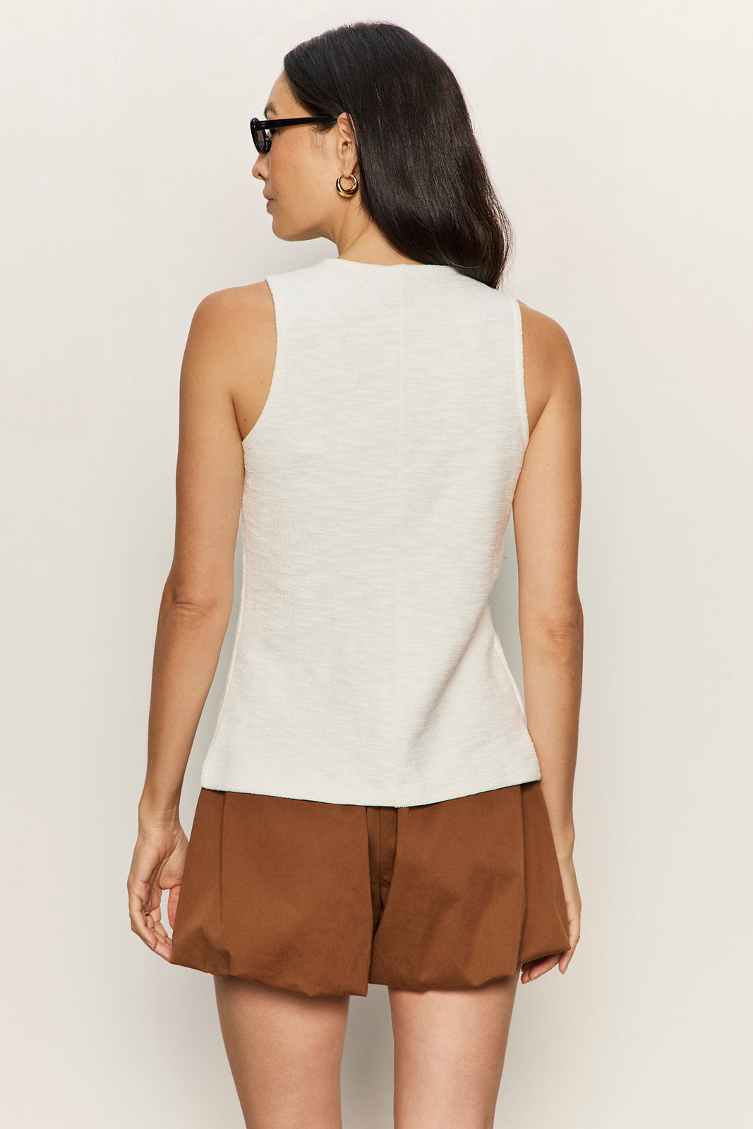 Woman wearing a white sleeveless top and brown shorts against a plain background
