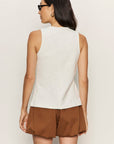 Woman wearing a white sleeveless top and brown shorts against a plain background