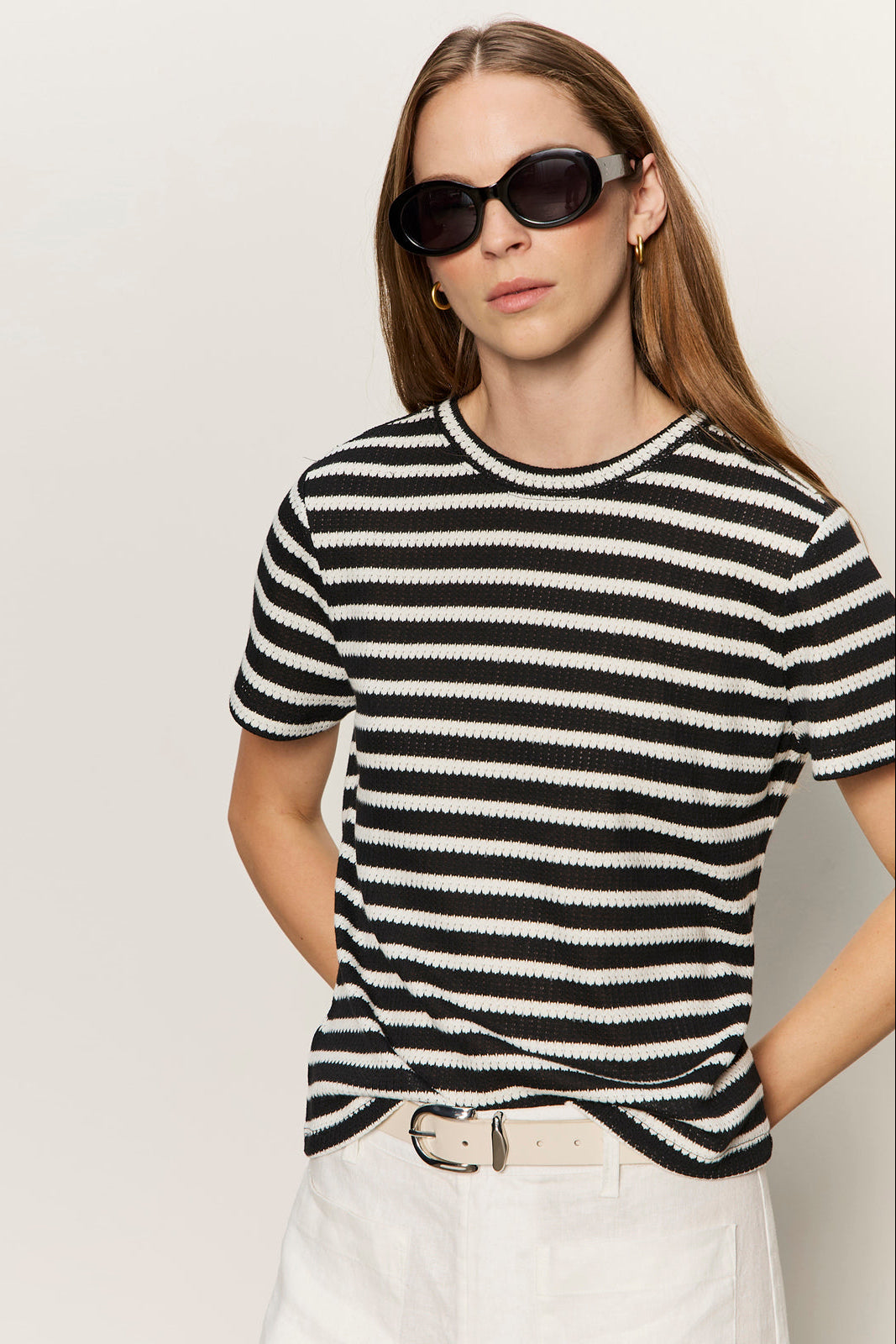 Woman wearing a black and white striped sweater with sunglasses on a plain background