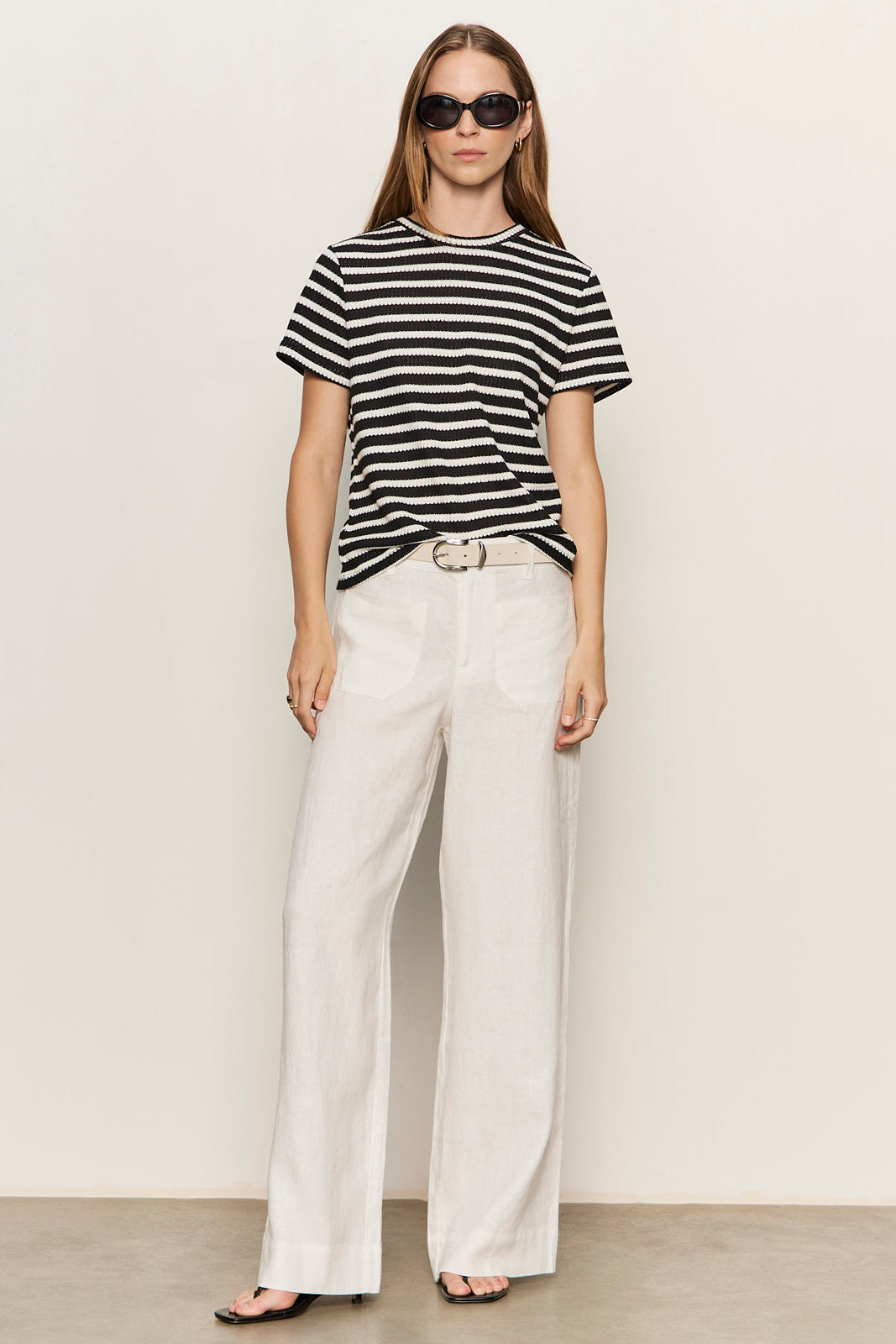 Woman wearing a black and white striped shirt and white pants against a plain background