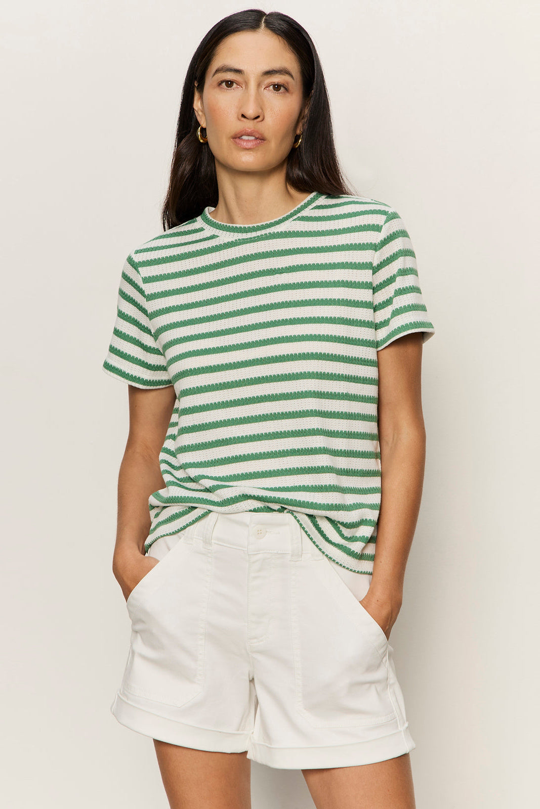 Woman wearing a green and white striped shirt and white shorts on a plain background