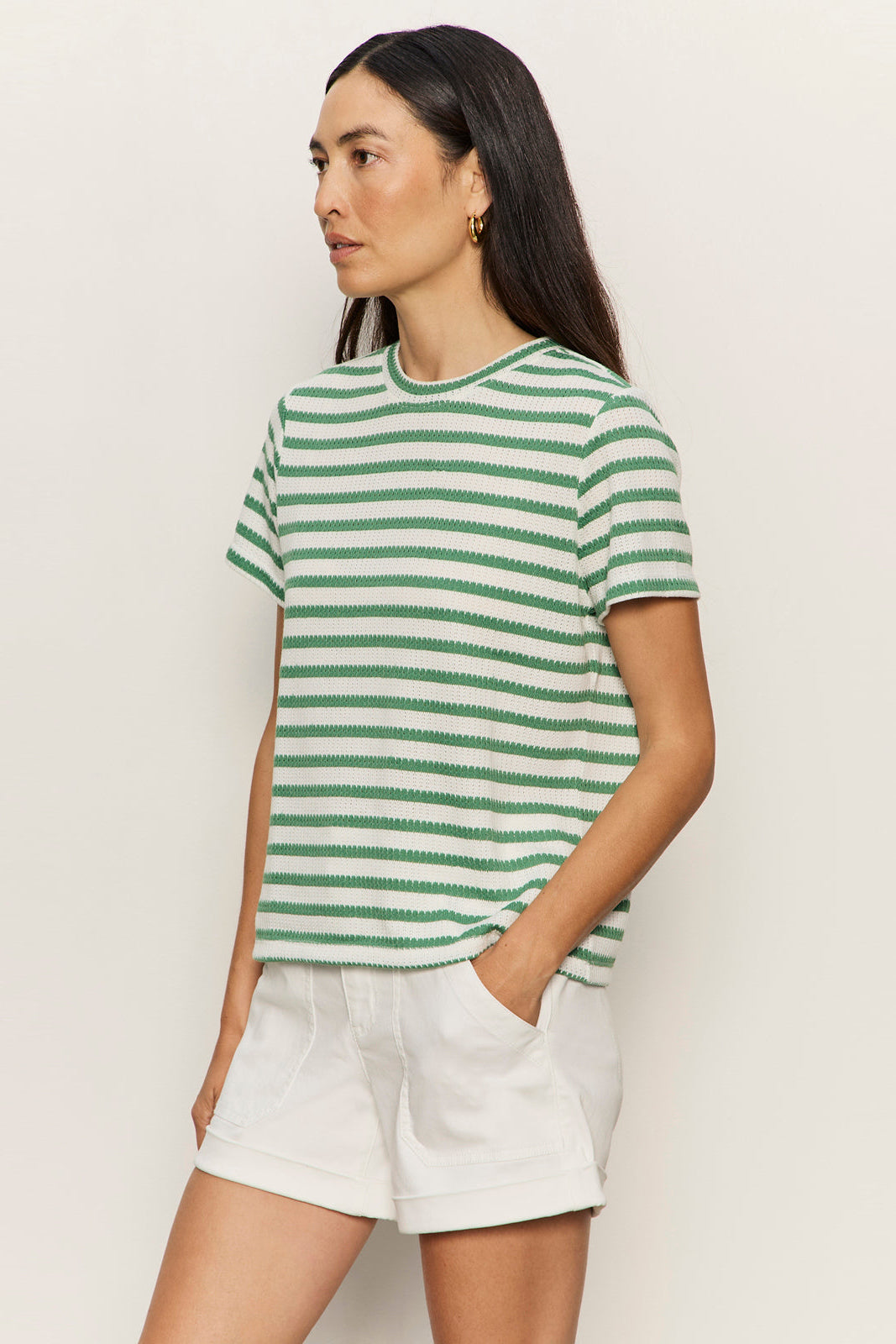 Woman wearing a green and white striped shirt and white shorts against a plain background