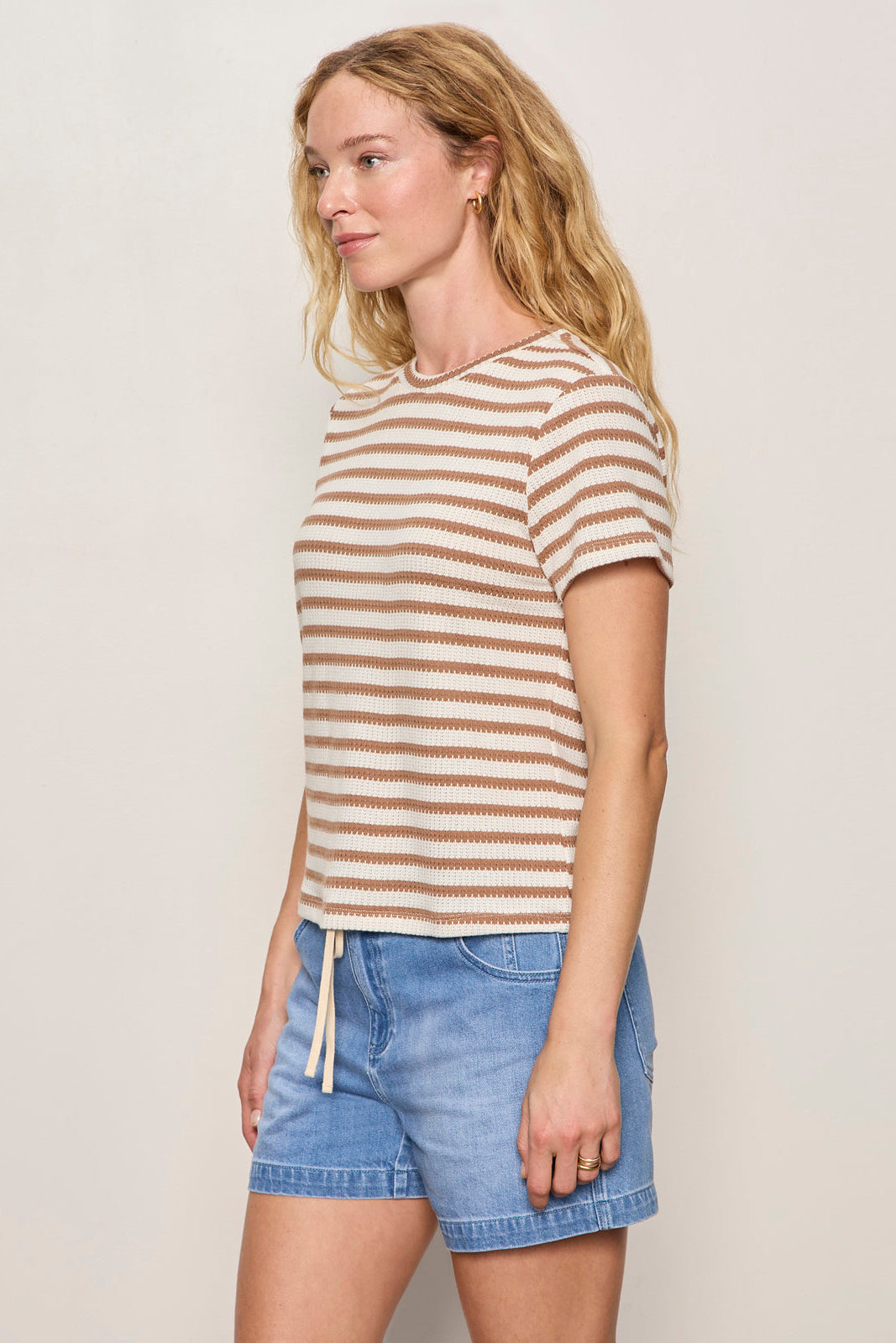Woman wearing a striped shirt and denim shorts against a plain background