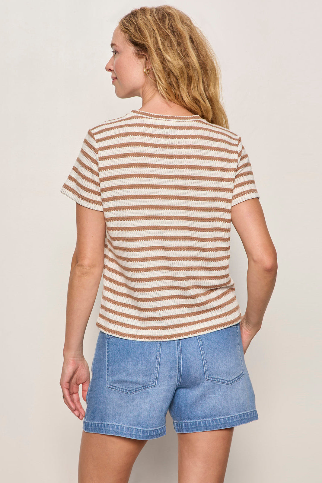 Woman wearing a striped shirt and denim shorts against a plain background