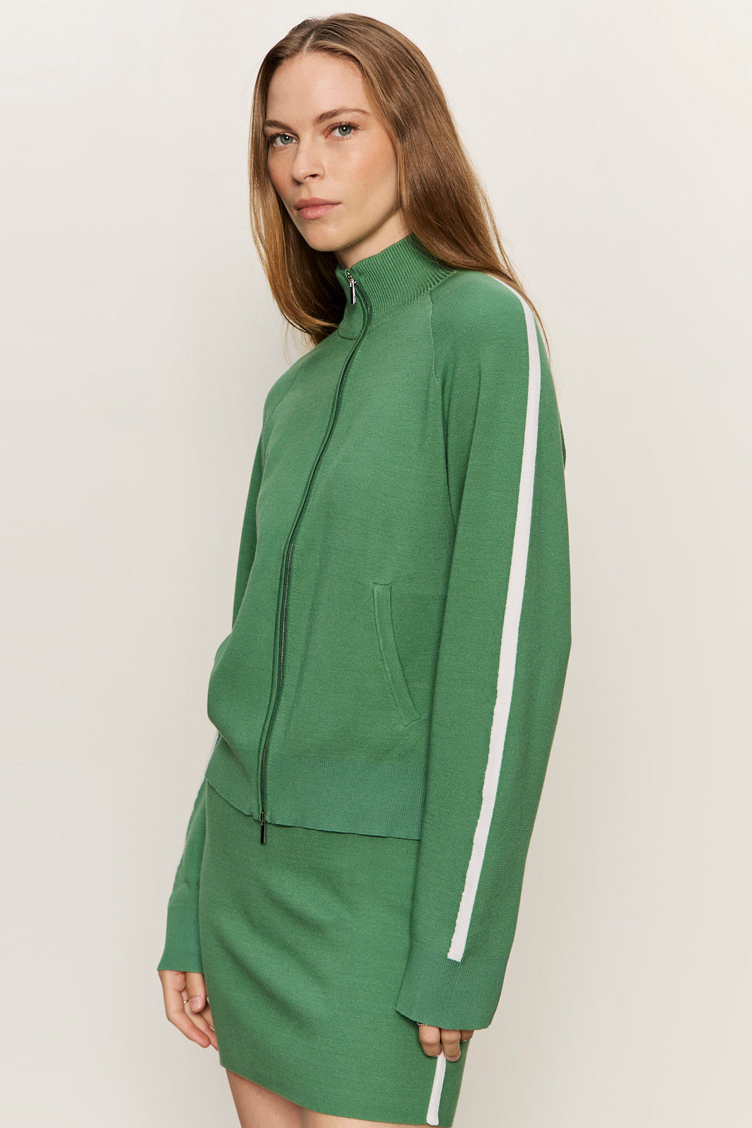 Woman wearing a green tracksuit with a white stripe on a plain background