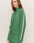Woman wearing a green tracksuit with a white stripe on a plain background