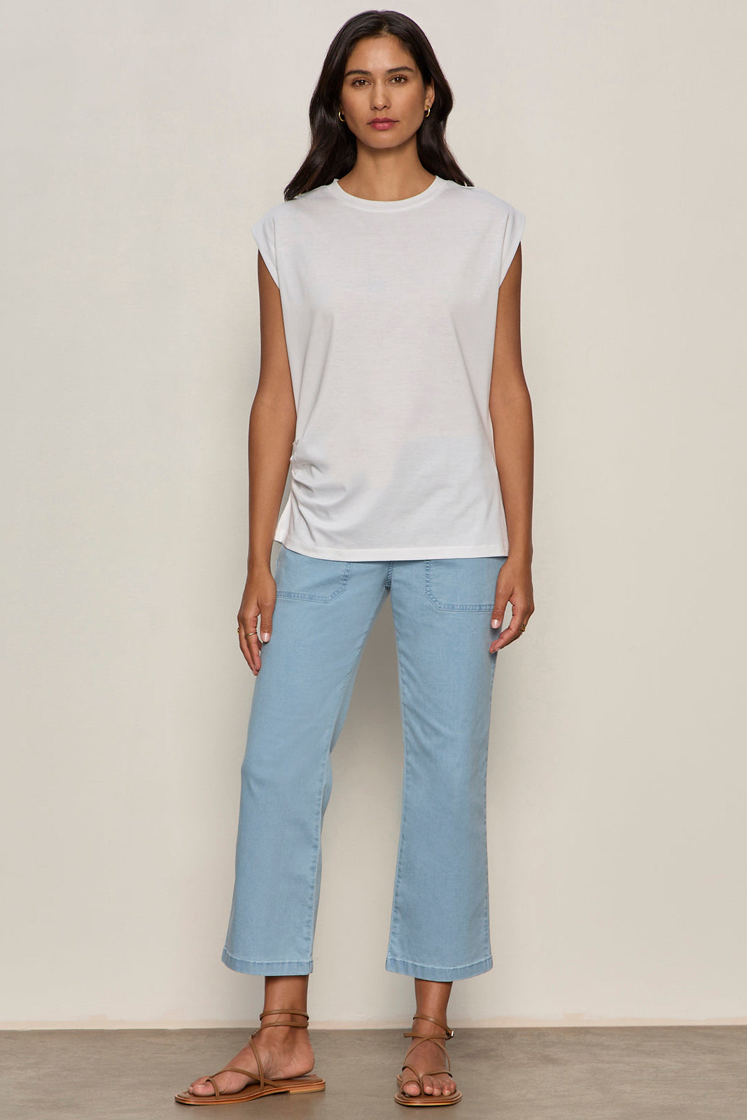 Woman wearing a white sleeveless top and light blue jeans against a plain background